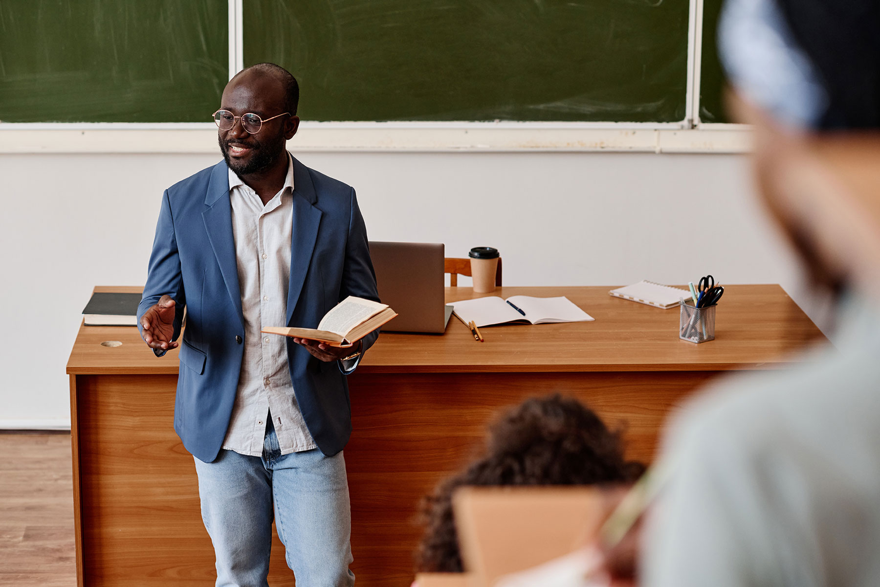 A professor standing in front of the classroom holding a book