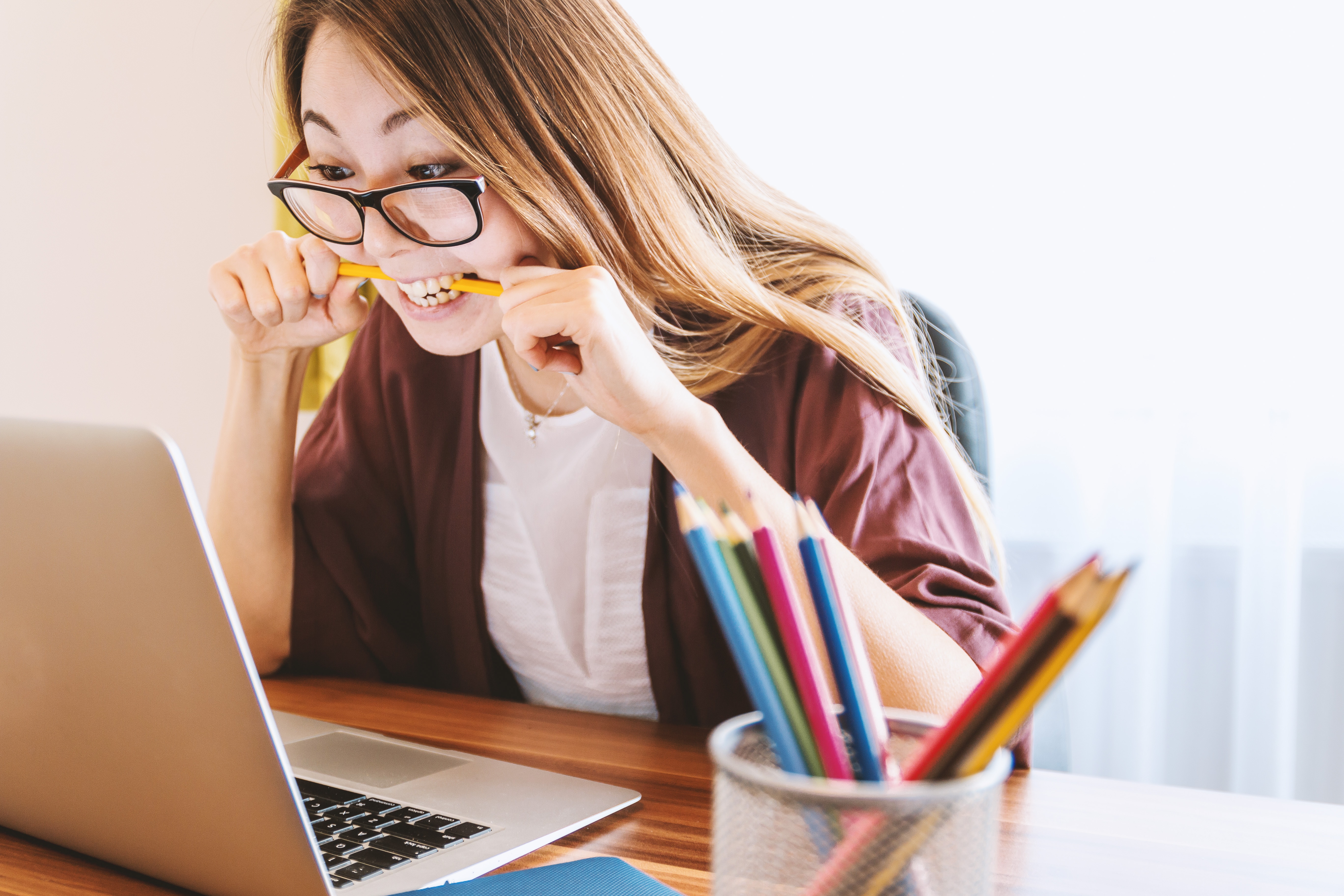 A student stressed out biting a pencil while looking into a laptop screen.