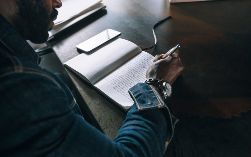 A person writting over handwritten notes in a notebook.