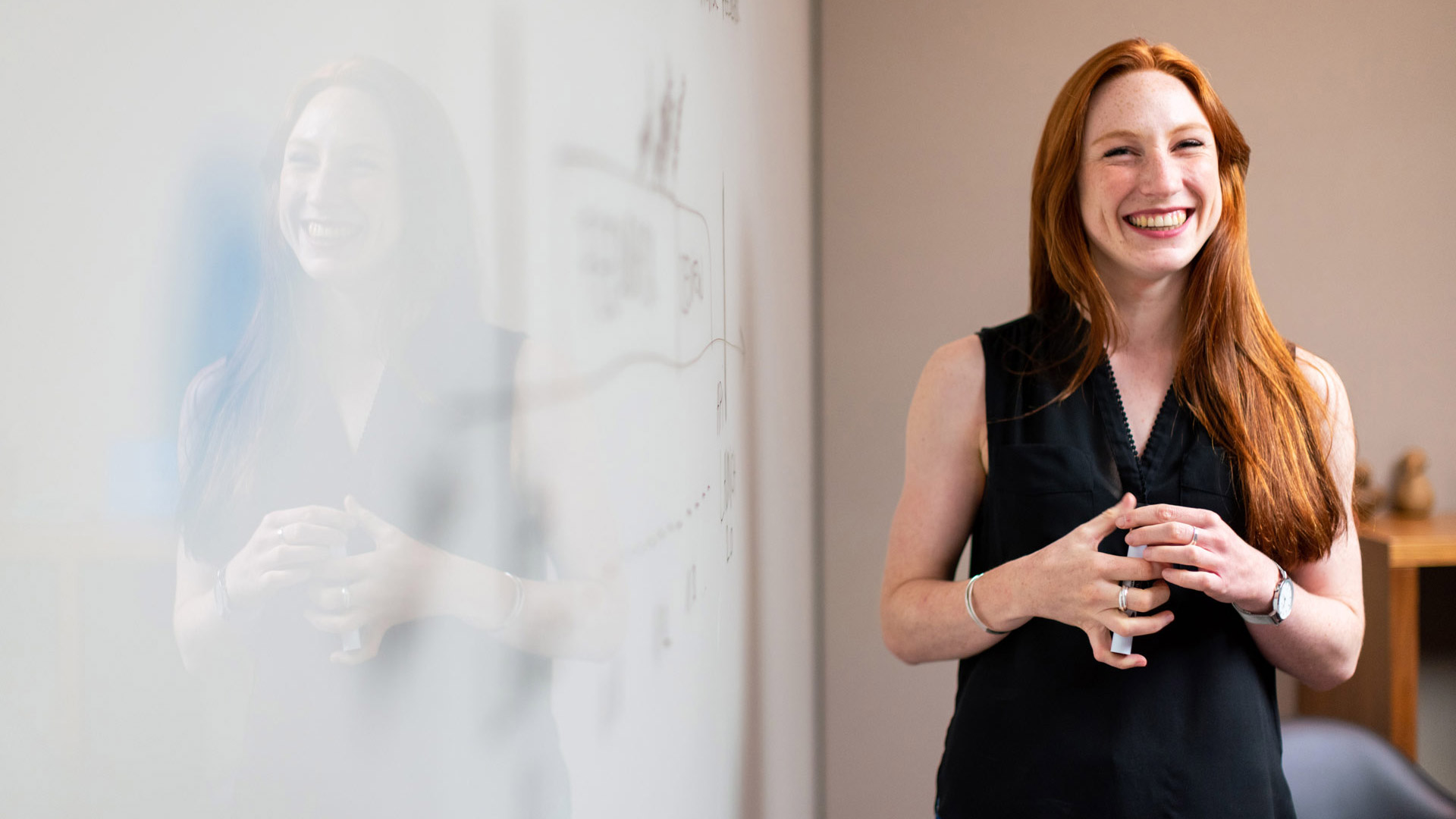 A person smiling in front of the white board and holding a marker.